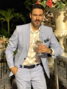 Caballero con traje celeste a la medida sosteniendo una copa.