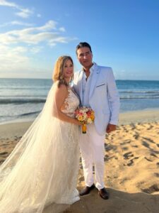 Pareja en la playa, novio viste traje color arena ligero.