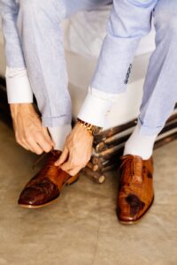 Detalle de zapatos de cuero café de novio preparándose en la playa.