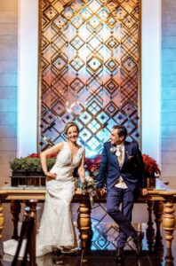 Novio sentado junto a muro decorado luciendo traje azul marino.