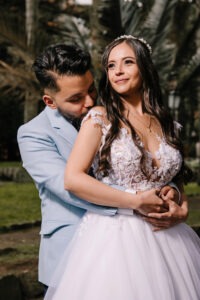 Novio abrazando a la novia en el campo con un traje azul claro a la medida.