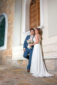 Novios posando en muro de piedra, él viste traje azul rey.