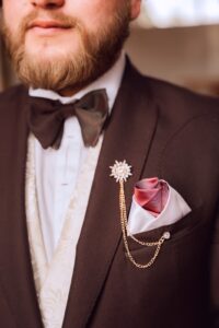 Acercamiento a traje café con corbatín oscuro y cadena de reloj de bolsillo.