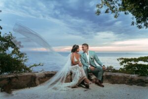 Novios sentados frente al mar, él con traje celeste de diseño.