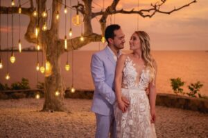 Novios bajo luces colgantes, él luce un traje azul claro bespoke.