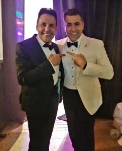 Dos hombres elegantes, uno con smoking negro y otro con smoking tropical.