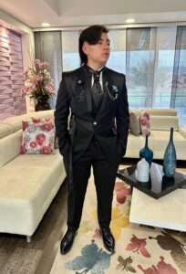 Novio de pie con traje negro y chaleco dorado.