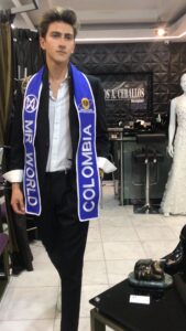 Cliente luciendo la banda de Mr. World Colombia con un traje sartorial.