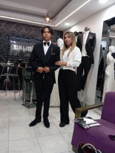 Hombre en traje negro formal acompañado de una mujer durante su visita al taller.