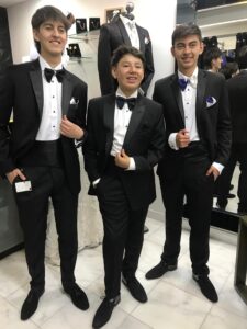 Padre e hijo posando en la boutique con impecables smokings negros coordinados.