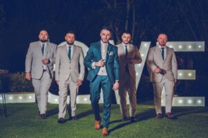 Novio y padrinos caminando al aire libre con trajes grises y azules.