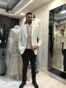 Caballero de pie en el atelier luciendo un traje negro clásico con corbatín.