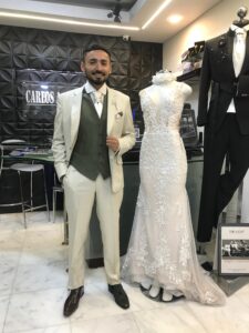 Novio modelando un traje verde oliva moderno y entallado junto a un maniquí.