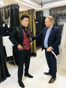 Carlos Ceballos asesorando a novio con traje negro y chaleco rojo de diseño exclusivo.