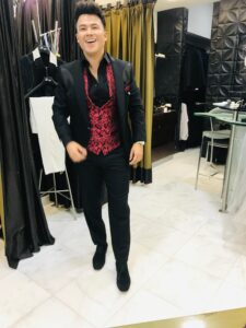 Novio caminando en el atelier con un traje negro y un audaz chaleco rojo brocado.